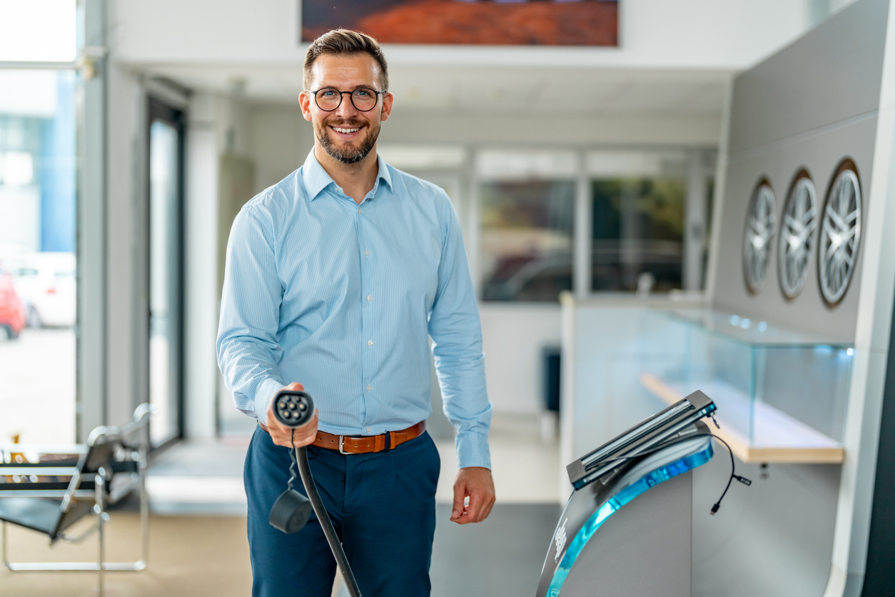 Portrait of a man standing with charging cable near the charging station.